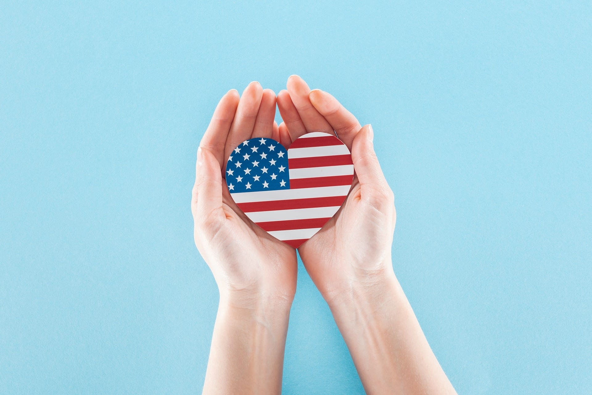 cropped view of woman holding heart made of national american flag on blue background