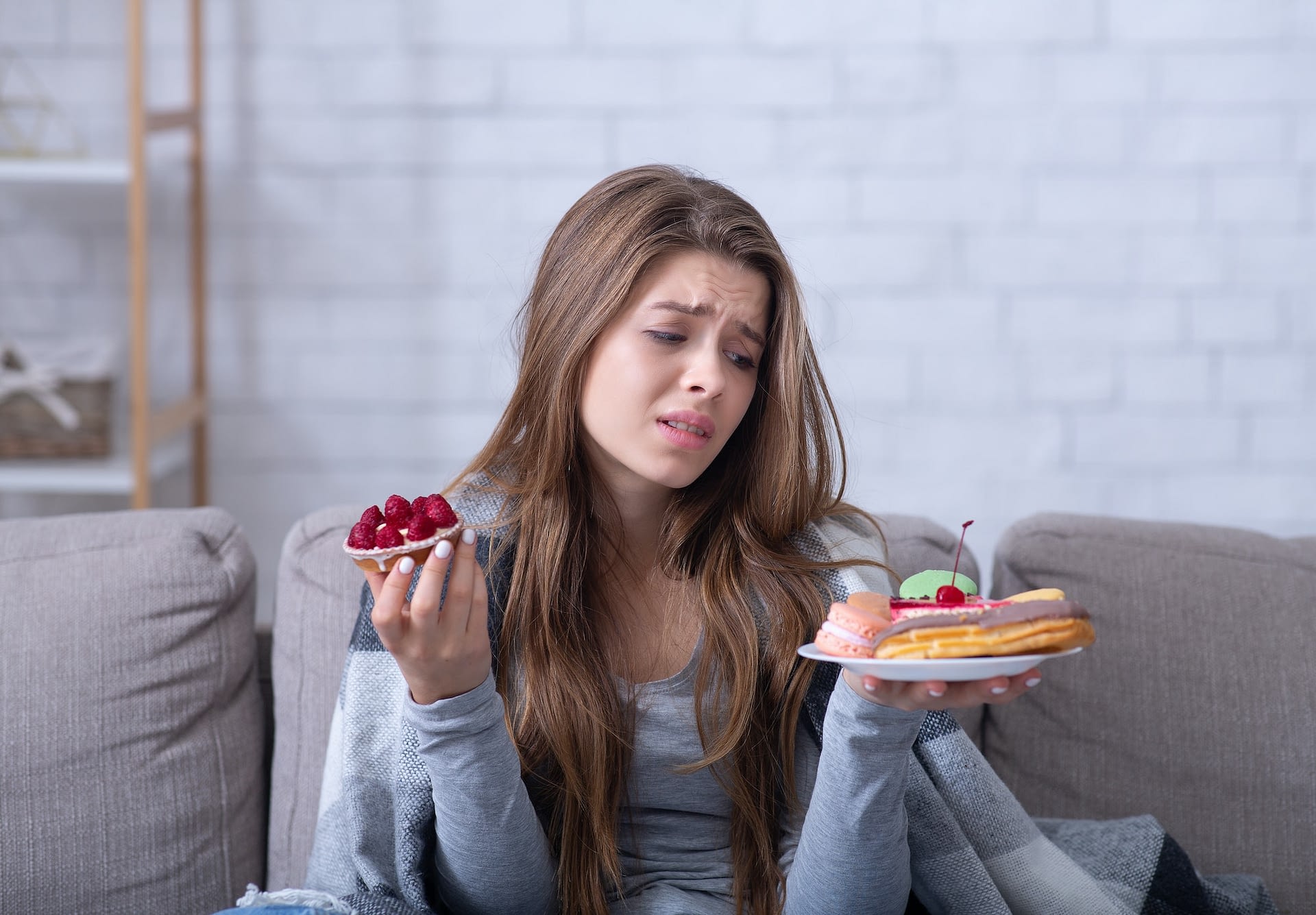 depressed young lady having eating disorder comforting herself with sweets on sofa at home