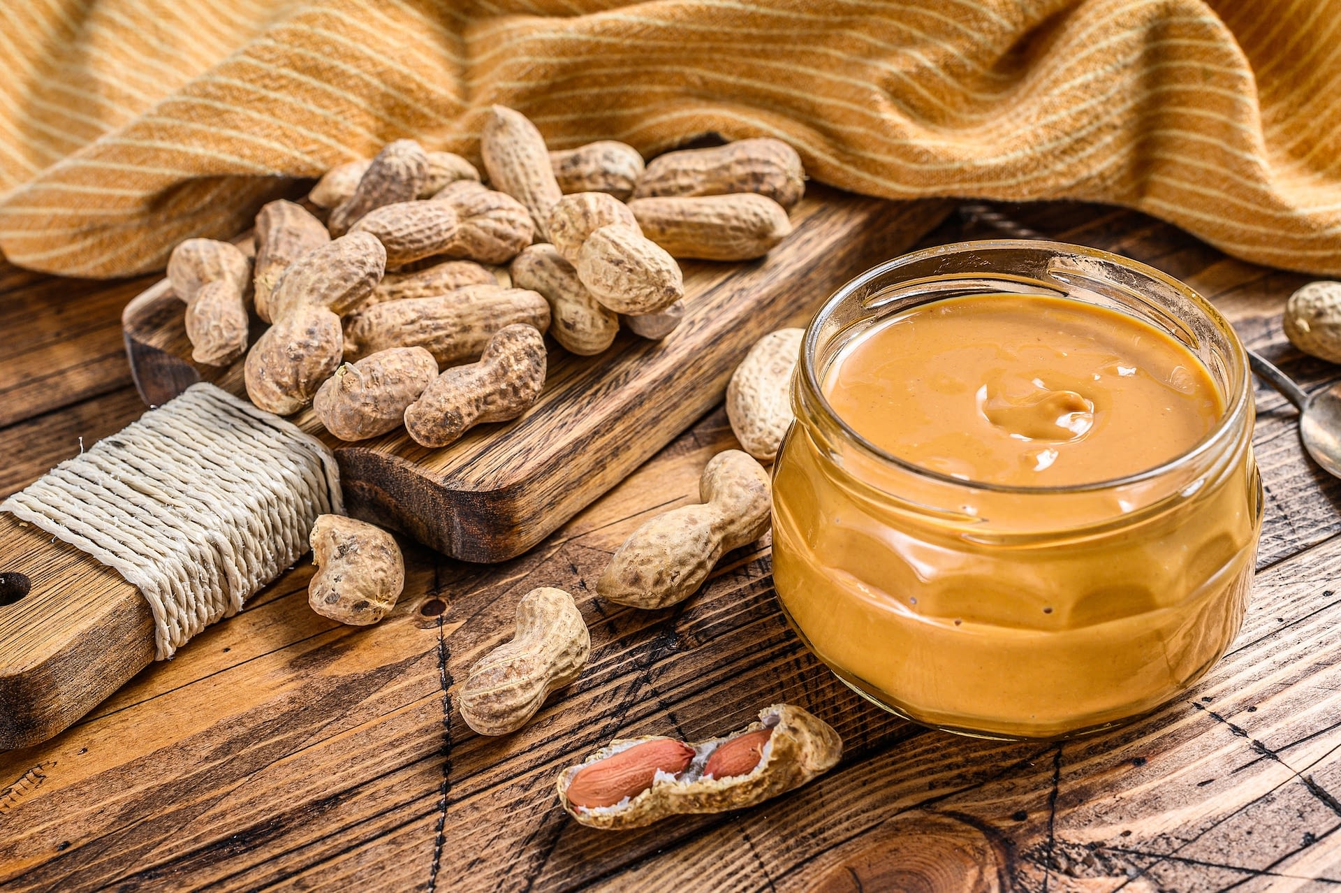 fresh made creamy peanut butter in a glass jar wooden background top view