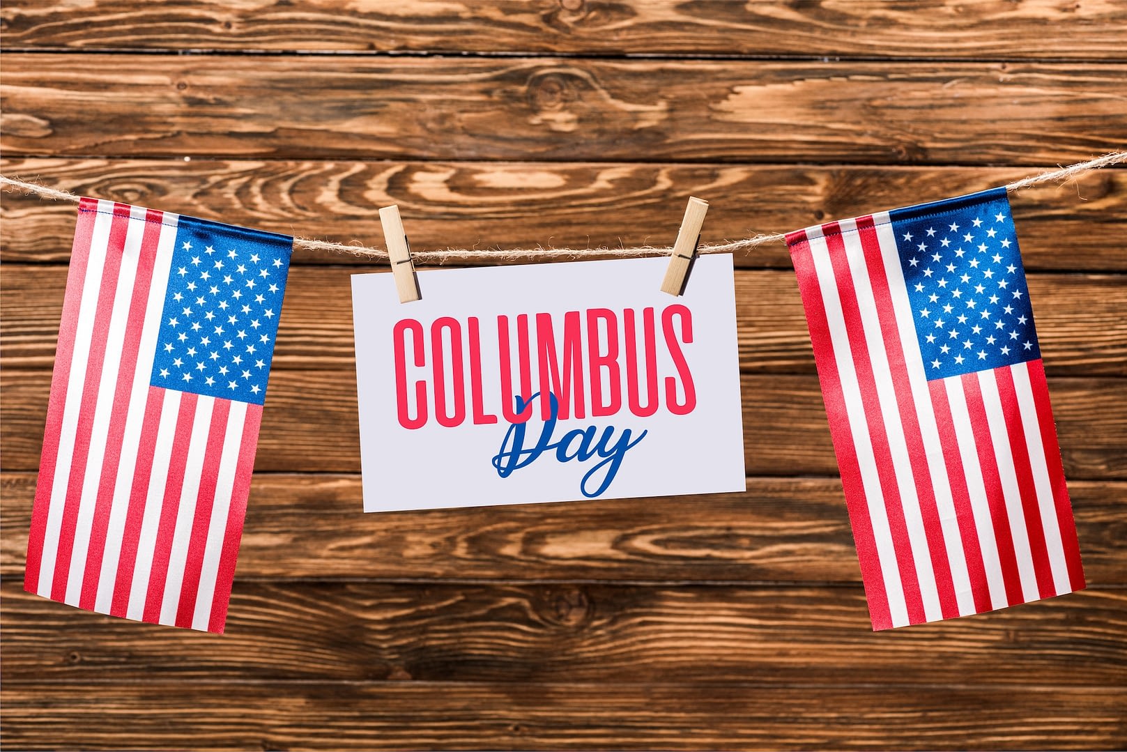 card with columbus day lettering hanging on string with pins and american flags on wooden background