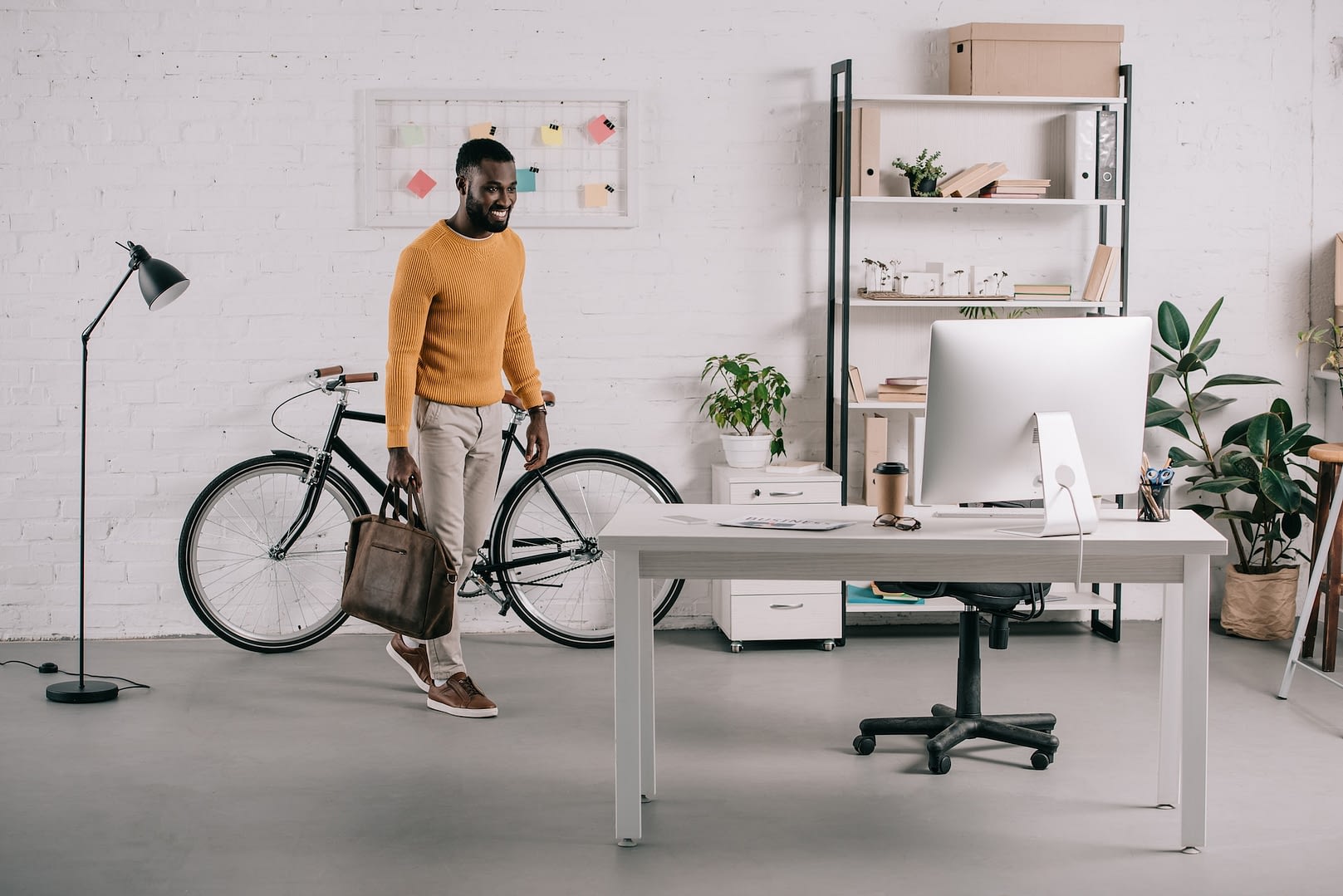 handsome african american designer in orange sweater entering office with briefcase