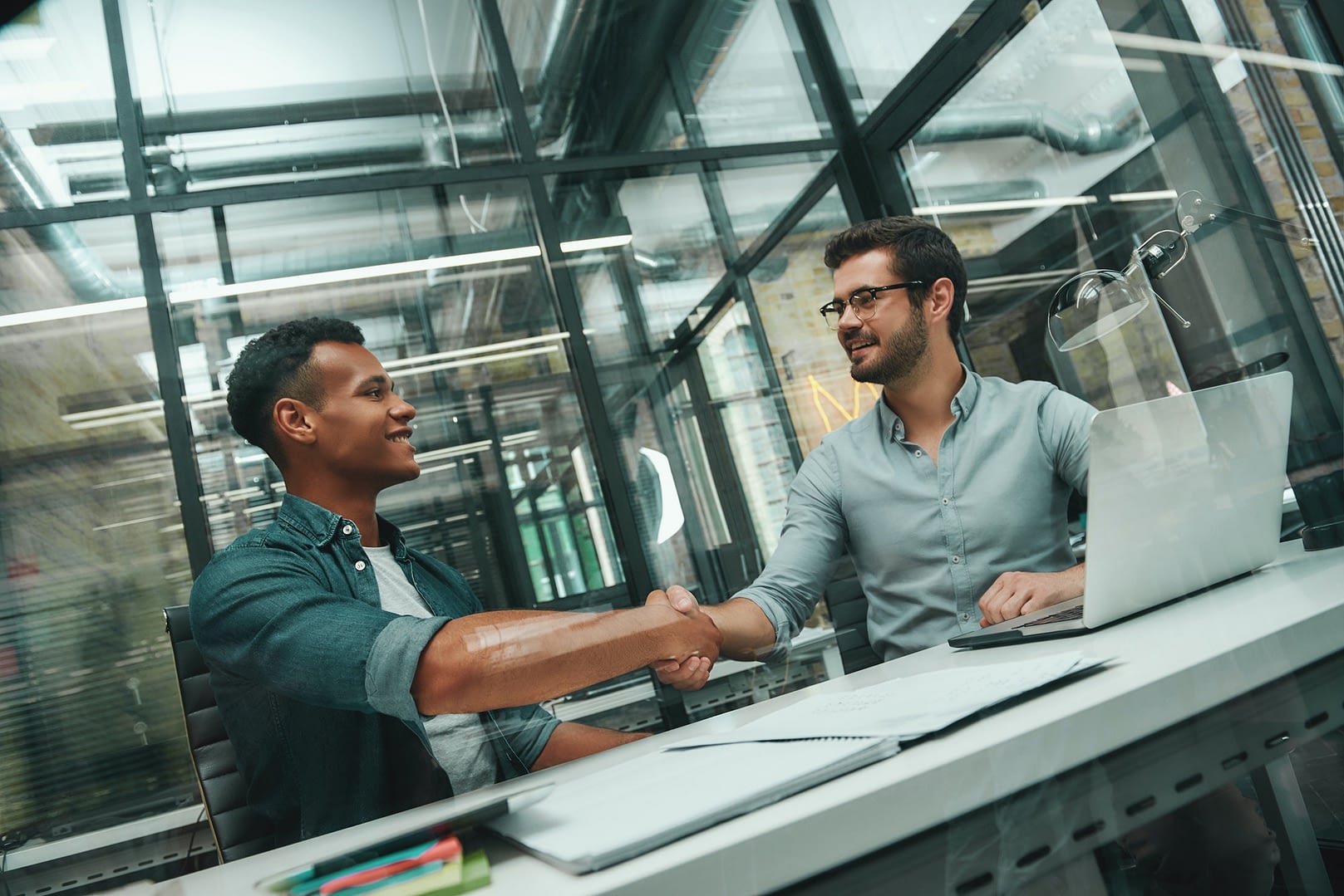 welcome on board two young and handsome men shaking hands and smiling while working in modern office