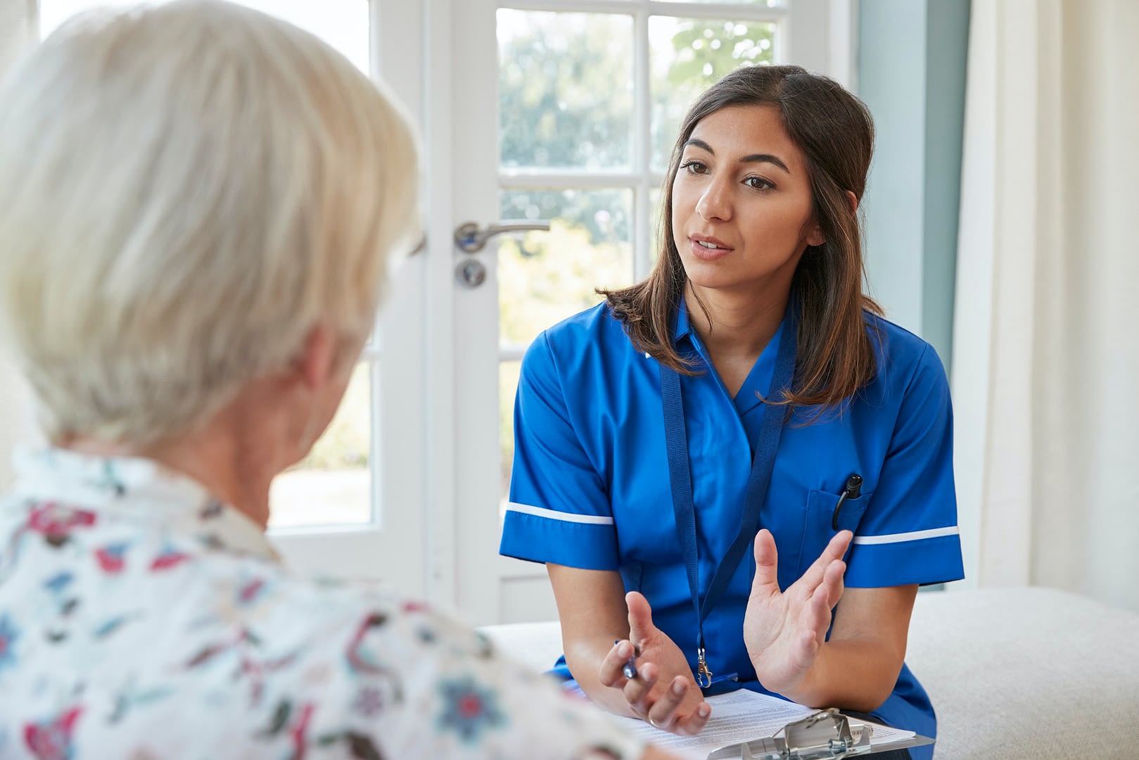 senior woman talking to young care nurse on home visit
