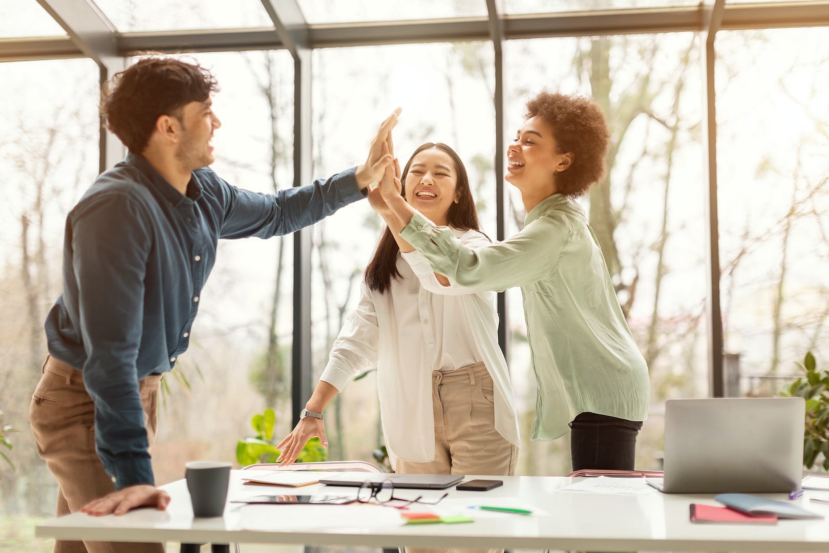 three coworkers giving high five sharing business success in office