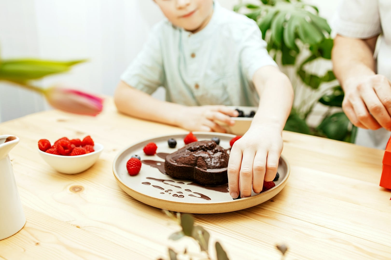 a boy decorates a heart shaped chocolate cake for mother s day with fresh berries valentine s day