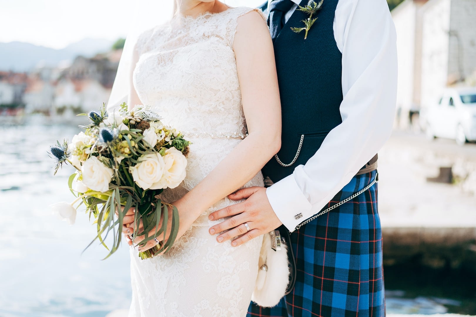 a bride in a wedding dress with bridal bouquet and a groom in a scottish national dress stand