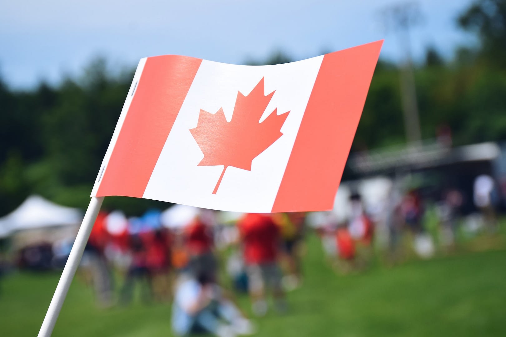 a canadian flag with blurred fairgrounds in the background happy canada day