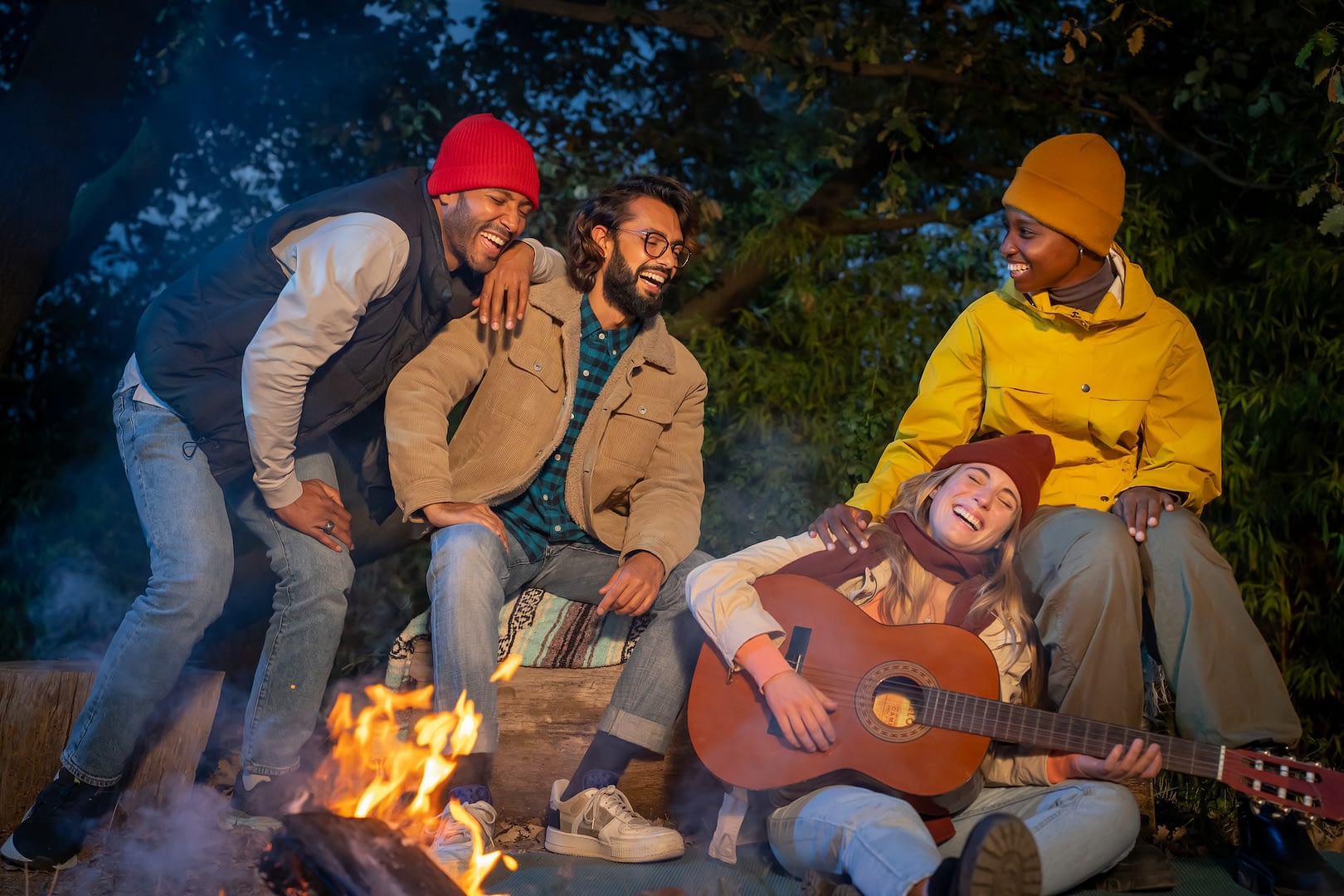 happy multiracial friends at campsite laughing playing the guitar at night enjoying the bonfire