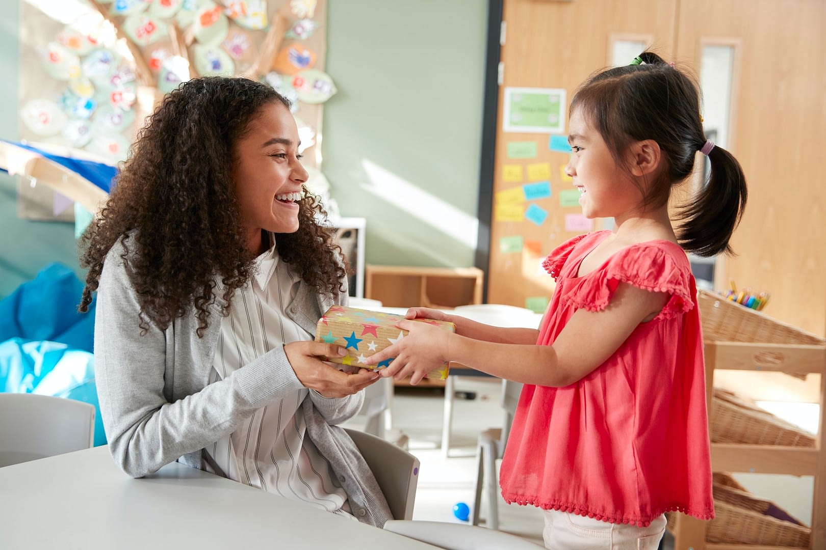 kindergarten schoolgirl giving a gift to her female teacher in a classroom side view close up
