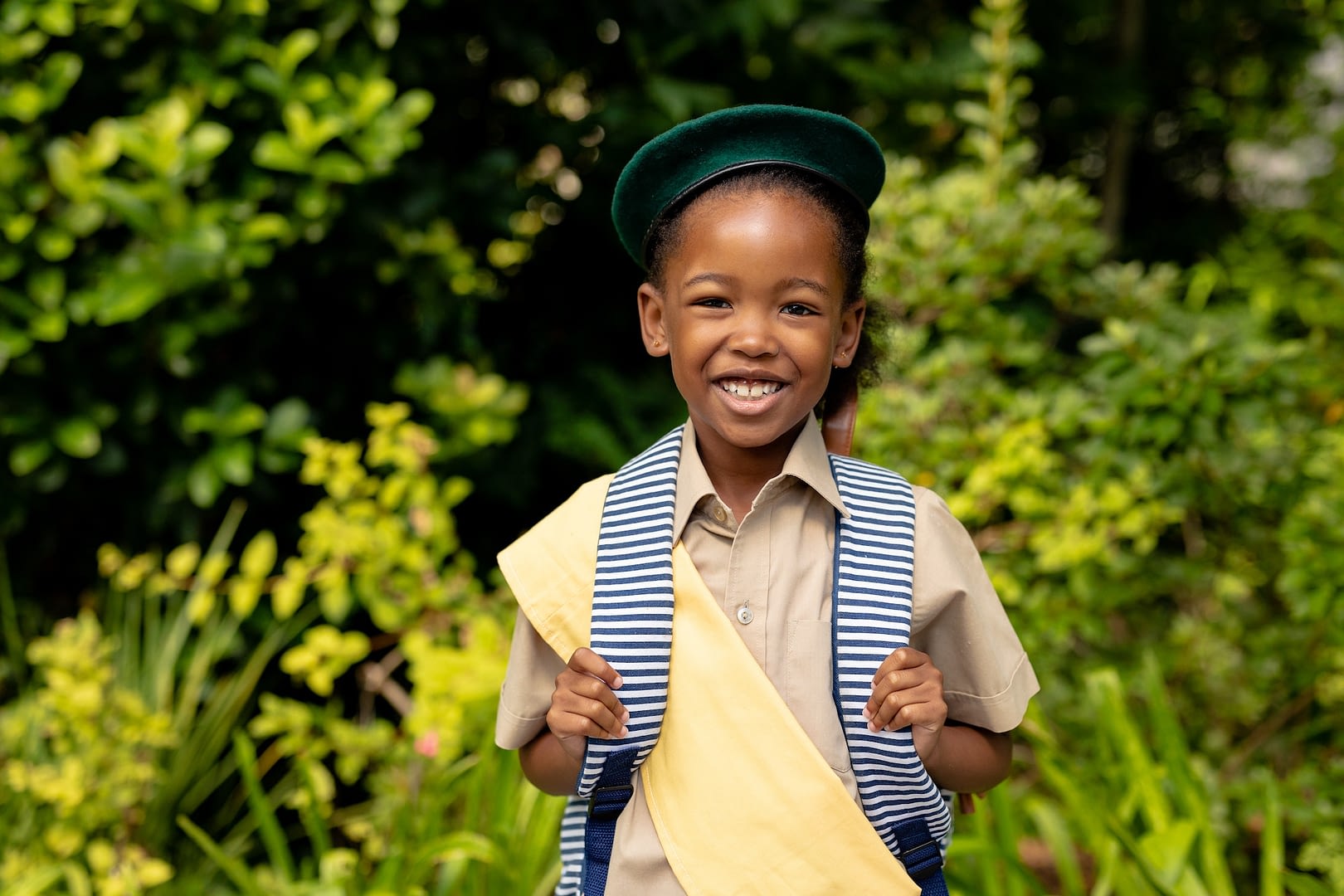 portrait of smiling african american scout girl in uniform with backpack against plants
