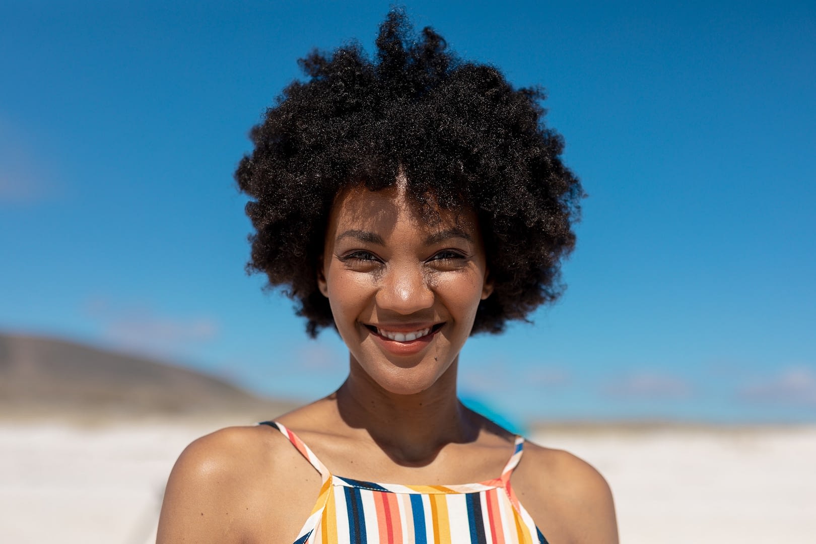 portrait of smiling african american woman with black afro hair at beach on sunny day