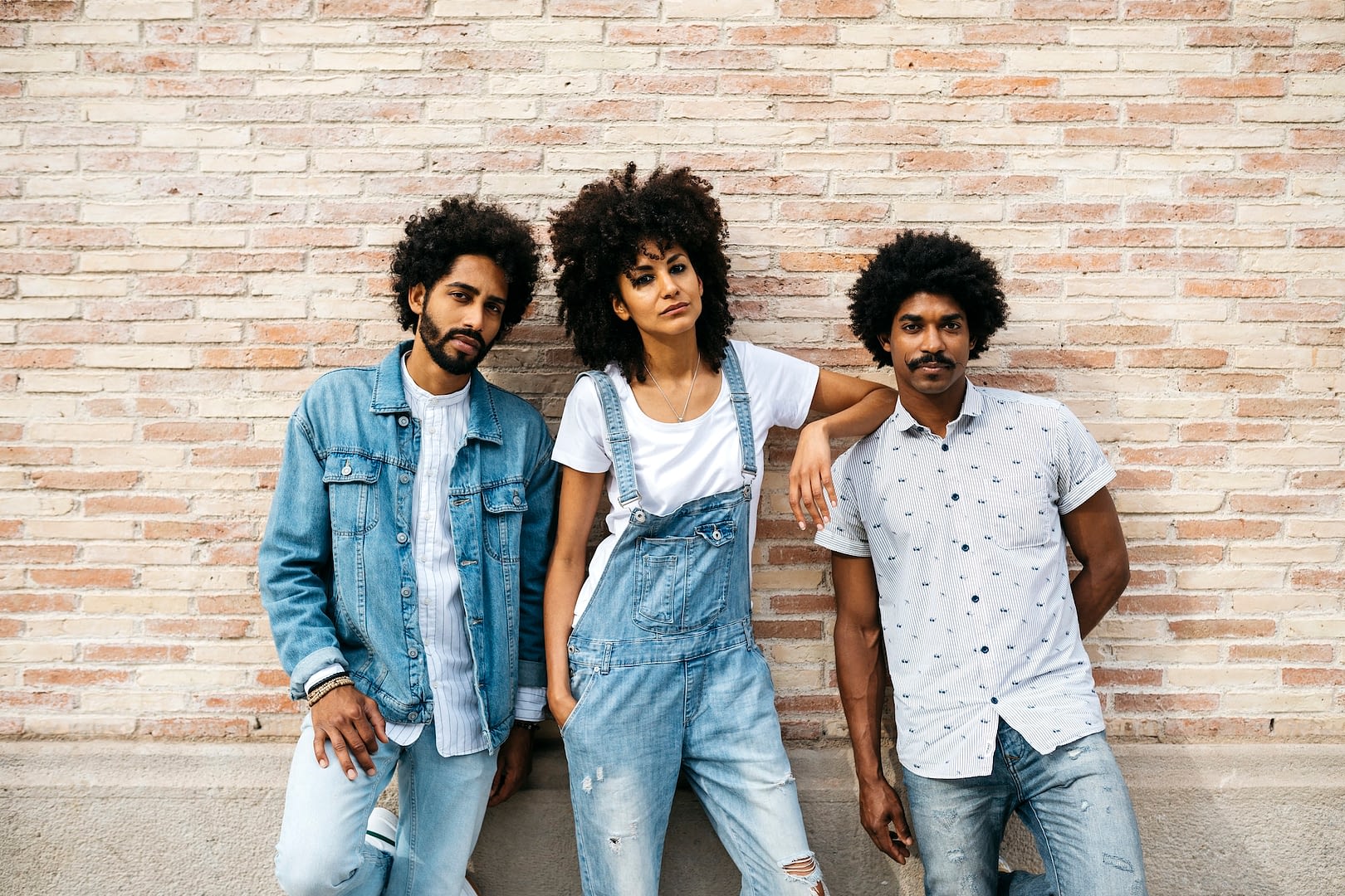 portrait of three friends wearing denim standing in front of brick wall