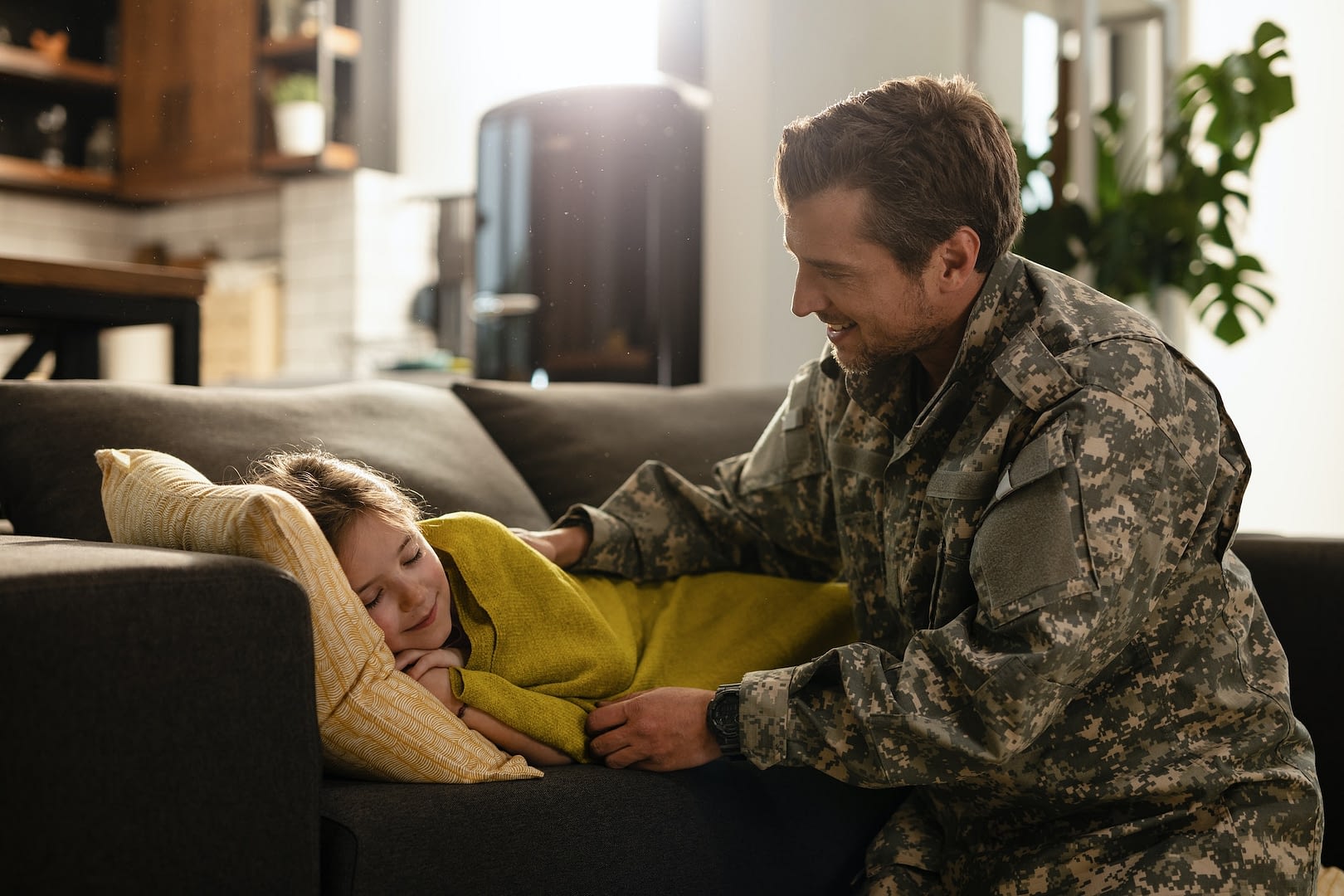 small girl sleeping carelessly on the sofa while military dad is next to her