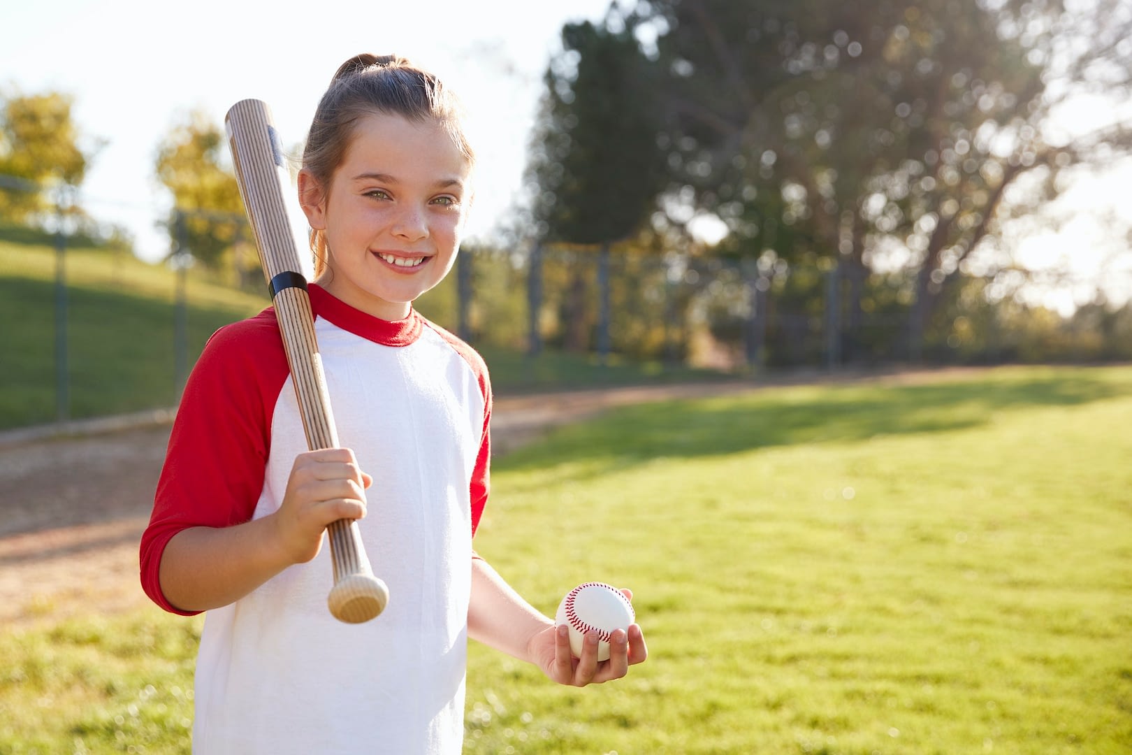 young girl holding baseball and baseball bat looks to camera