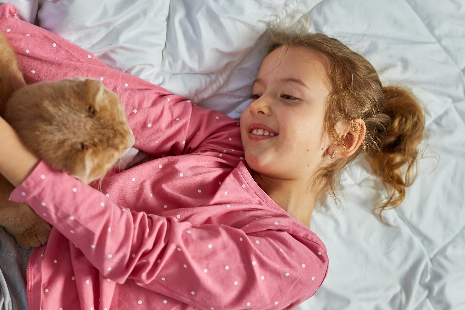 cute ginger cat and little girl lying on a soft blanket in bed