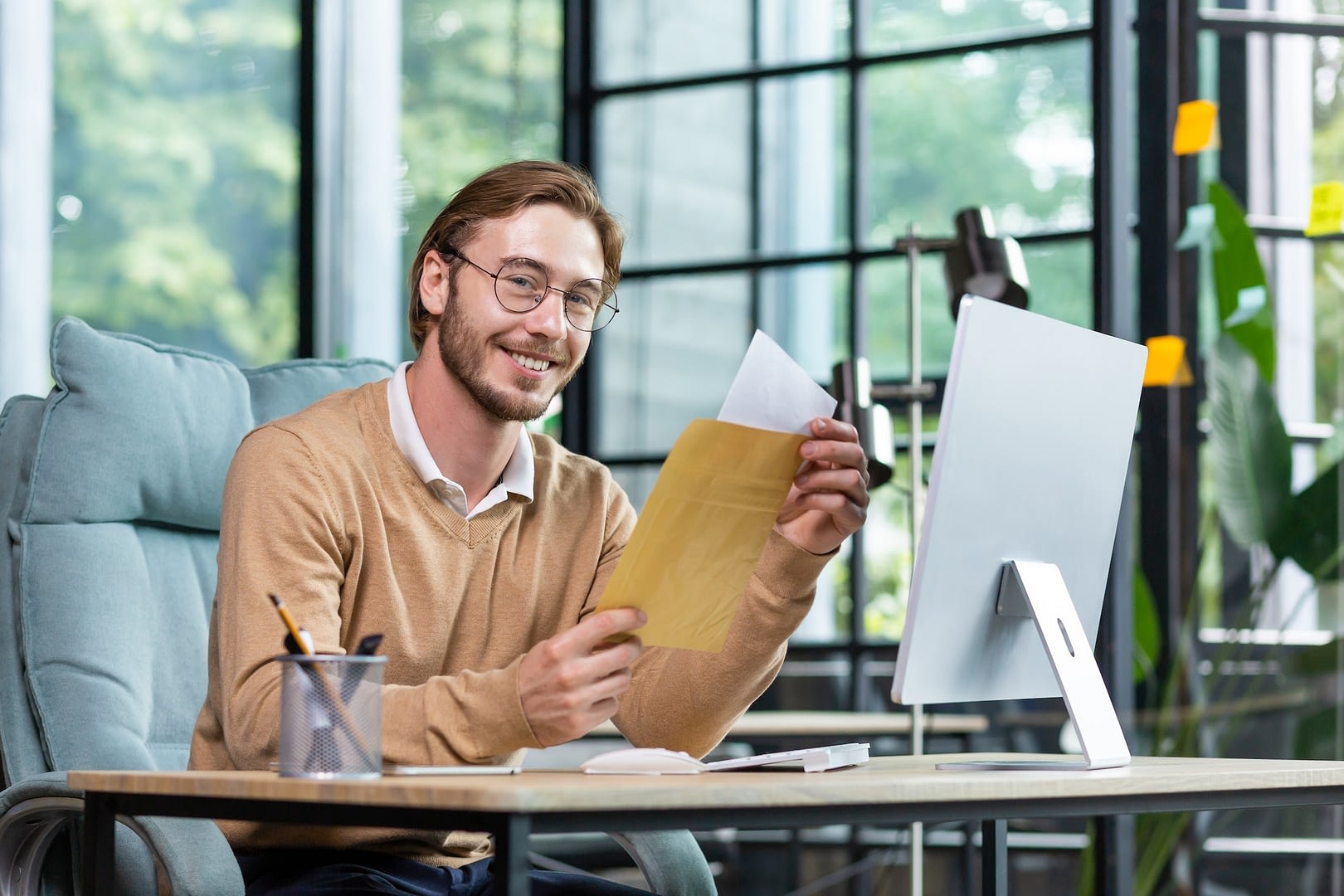 a young male businessman sits in the office received and holds an envelope with a letter in his