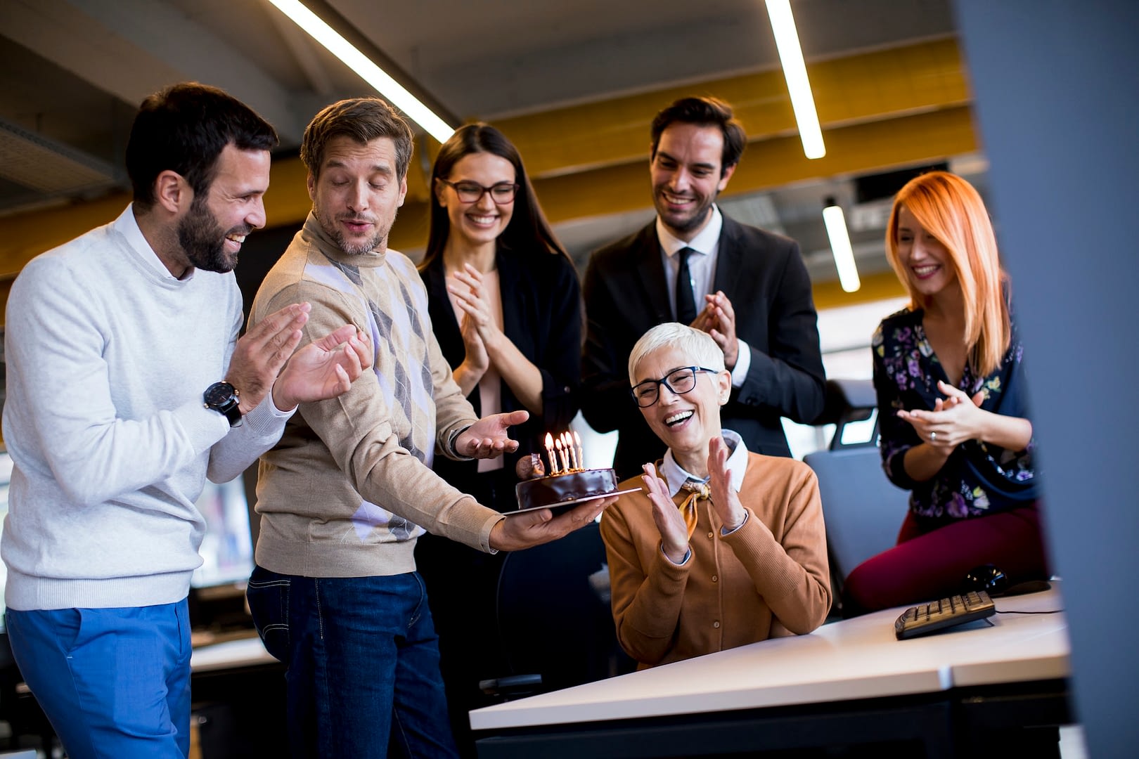 young colleagues celebrate an older colleague s birthday at the office and bring a cake