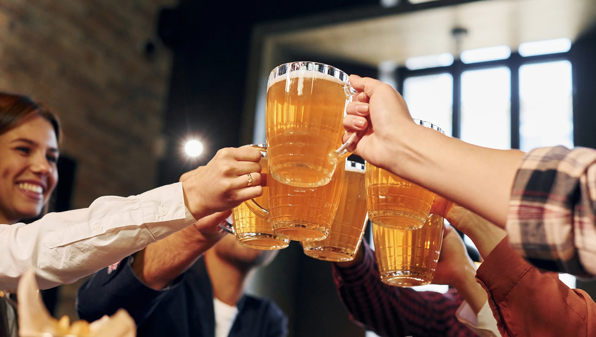 cheering together group of young friends sitting in bar with beer