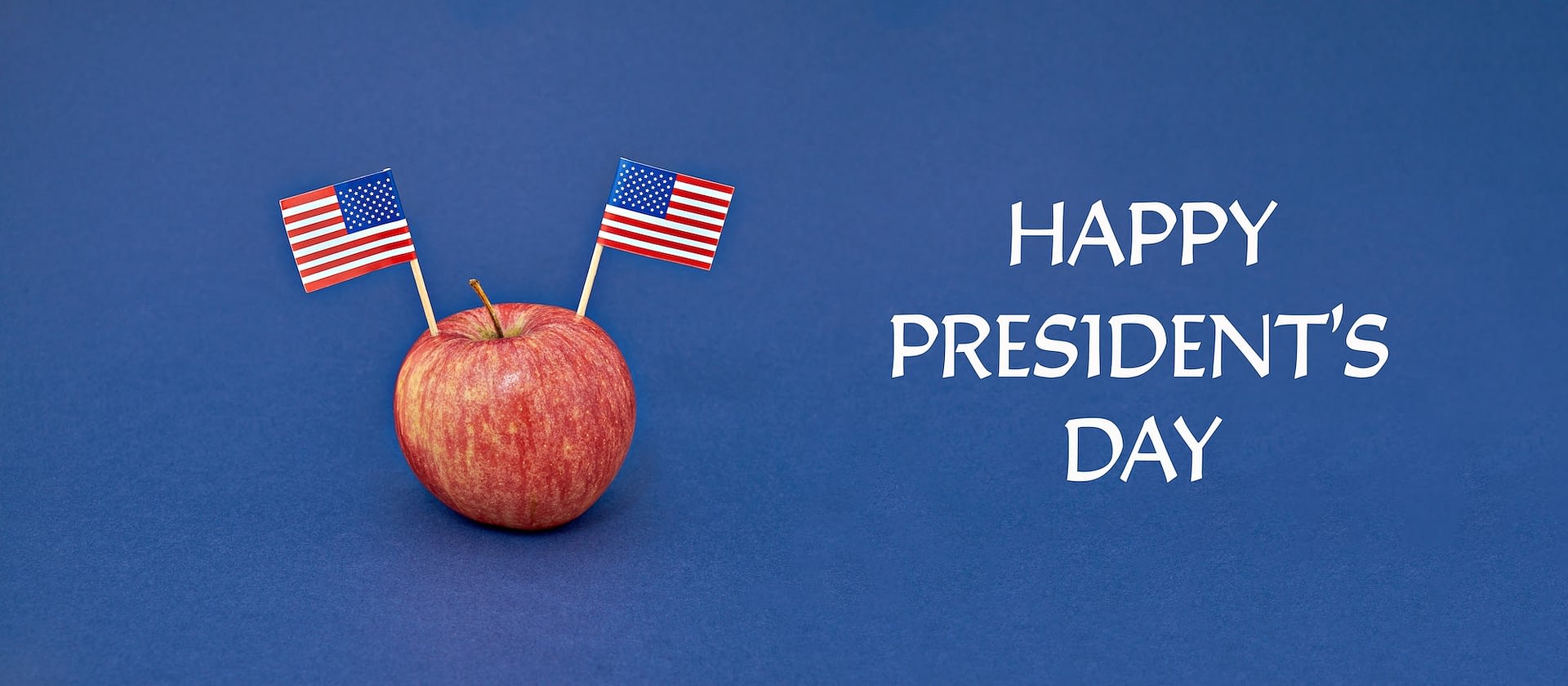 red apple with two flags of usa on blue background greeting card to celebrate happy presidents day