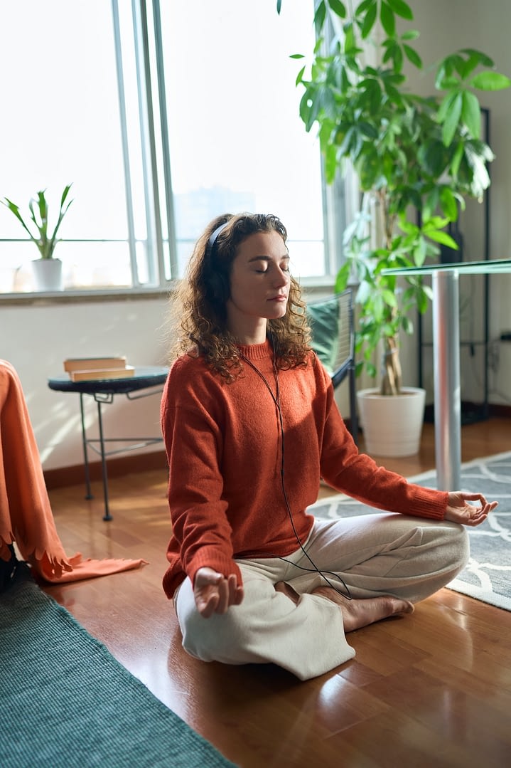 young mindful woman wearing headphones doing meditation at home vertical