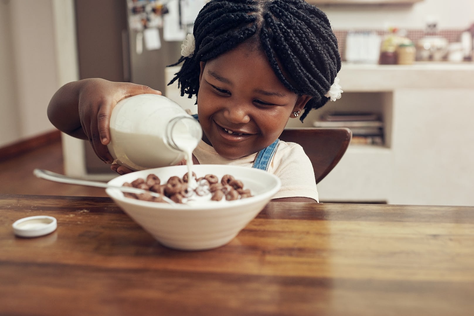 cropped shot of an adorable little girl pouring milk into her cereal bowl at home