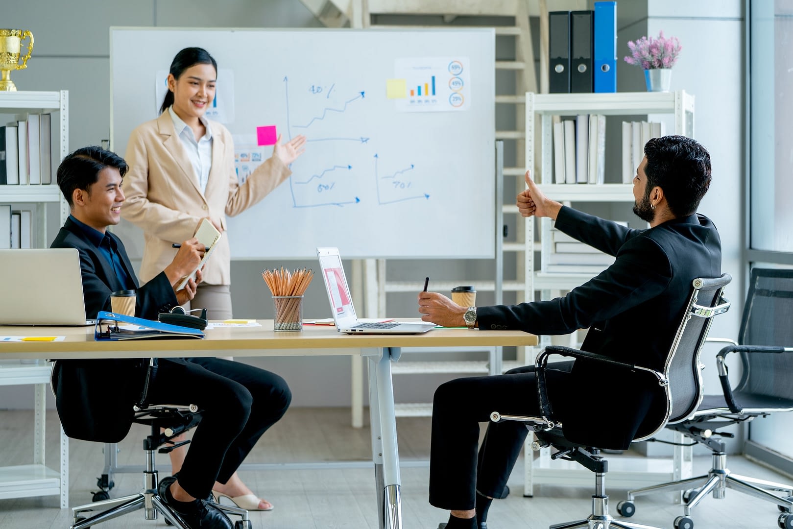 asian manager point to project on board that present by pretty business woman in meeting room